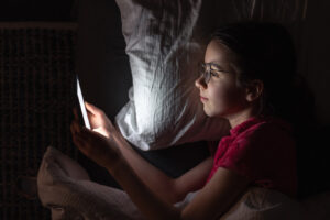 A teenage girl with a smartphone lies in bed at night, top view.